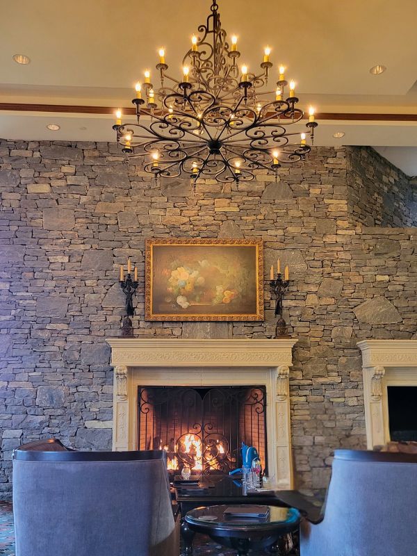 A fireplace in a stone wall in the Biltmore Inn's Library Lounge with chandelier over blue chairs