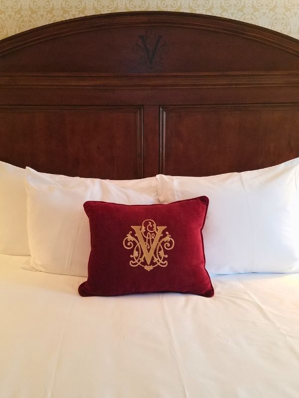 A king bed at The Inn at Biltmore with red pillow with Vanderbilt emblem